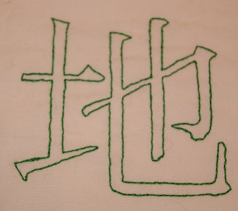 Rückstich-Beispiel: Das Kanji für Boden in grünem Rückstich auf Popeline, Vorlage in Pinselschrift. Vorderseite.